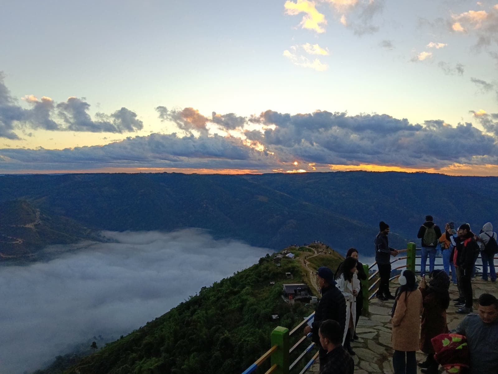 Travellers watching the sunset from a Meghalaya hilltop viewpoint above the clouds